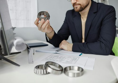 Engineer at workplace reviewing blueprints and holding machine part